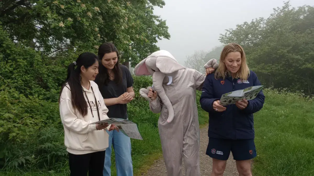 Two students, one staff member, and a person dressed in an elephant costume standing on a footpath near Blackford Hill