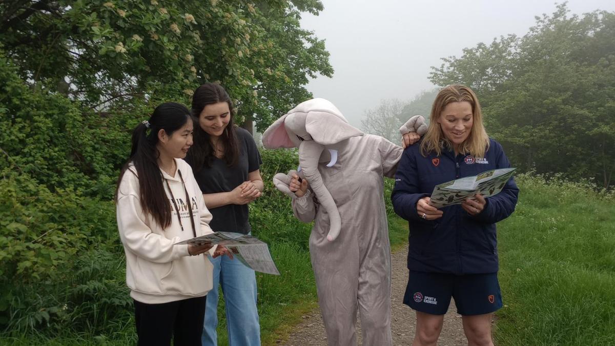 Two students, one staff member, and a person dressed in an elephant costume standing on a footpath near Blackford Hill