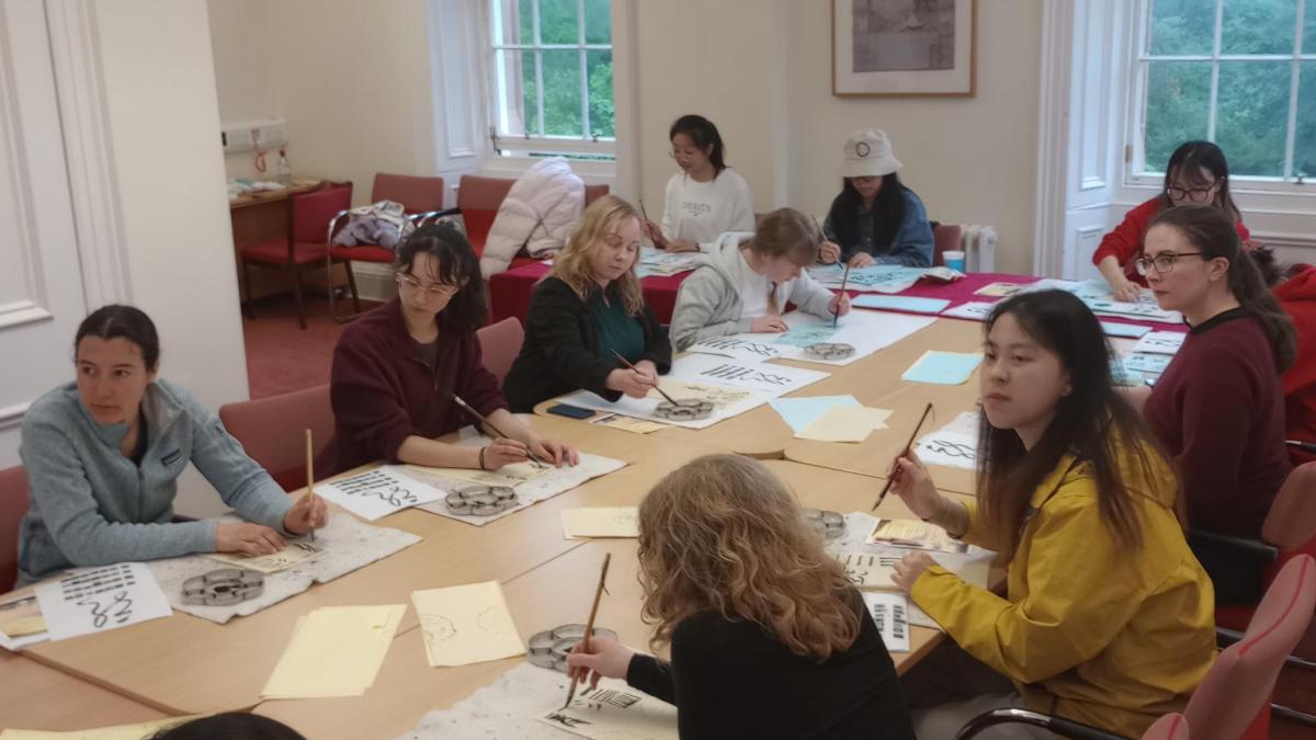 Photo of students sitting at a long table learning Chinese calligraphy