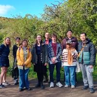 9 people standing in a line outside on a walking path on a sunny day