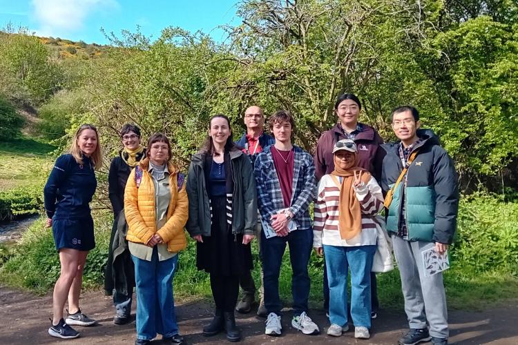 9 people standing in a line outside on a walking path on a sunny day