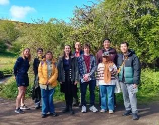 9 people standing in a line outside on a walking path on a sunny day