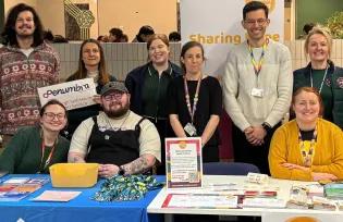 Group of people standing and sitting behind large table that has signs and leaflets on it