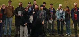 Group photo of students and Chris, wellbeing adviser, standing outside, in front of a grass field 