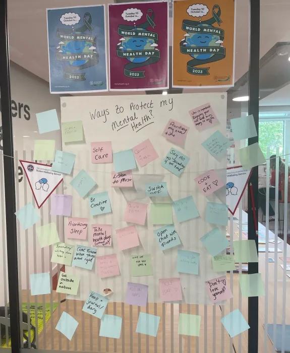 A glass wall covered with post it notes with writing on them under the title 'Ways to protect my mental health'
